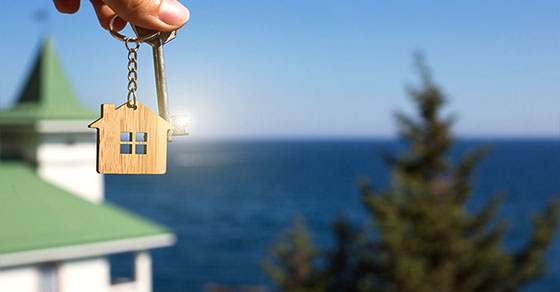 person holding house shaped keychain and looking at lake