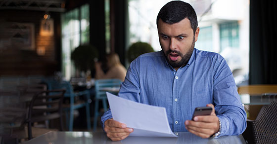 image of shocked man looking at a piece of paper and holding a cell phone