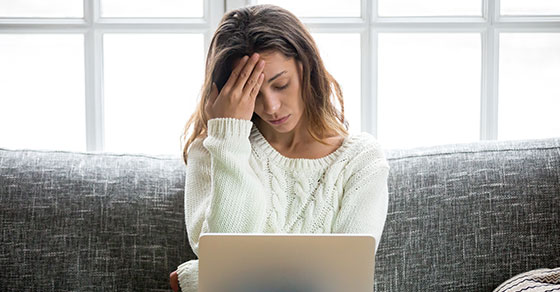 woman in white sweater looking distraught with a laptop